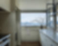 Modern kitchen with large window overlooking mountains and water.
