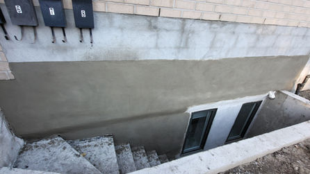 Exterior view of a basement entrance with steps and windows.