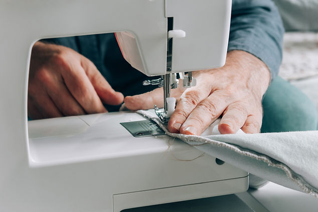 An elderly tailor man sews on a sewing machine