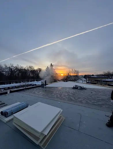 Toit enneigé avec coucher de soleil et traînée d'avion.