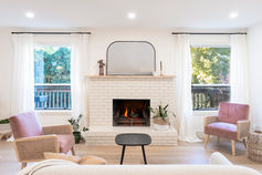 Bright living room with fireplace, pink armchairs, and large windows.