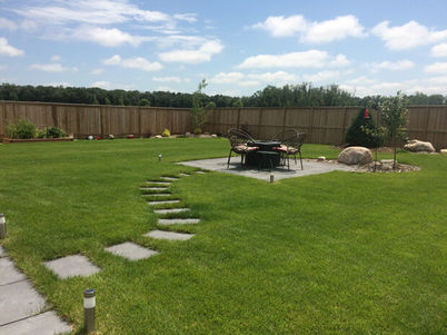 Green lawn with stepping stones leading to sitting area and wooden fence backdrop.