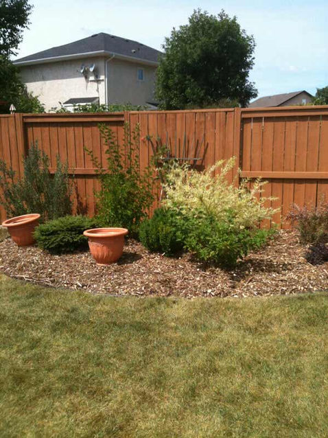 Wooden fence with plants, pots, and Mulch and Decorative Stone in a yard
