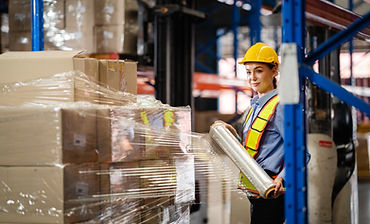 Female worker wrapped a parcel of stretch film on a cargo in a large factory warehouse