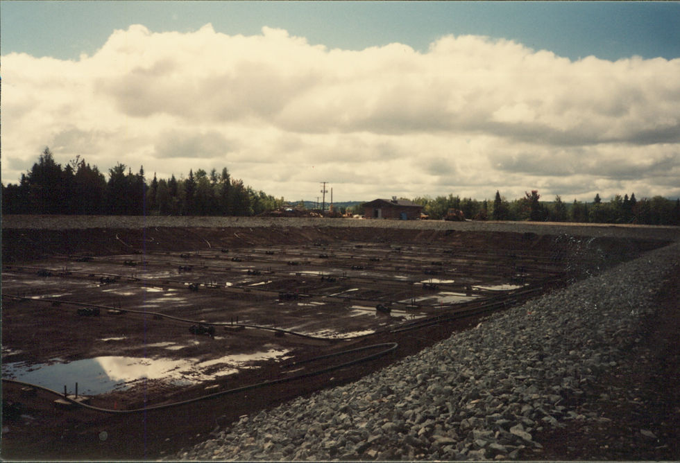 Vaste excavation boueuse avec talus de pierre et arbres à l'horizon.