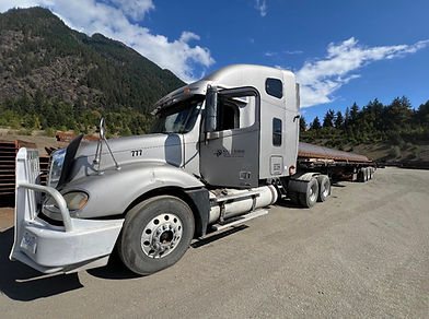 Silver semi truck with flatbed trailer in mountain setting