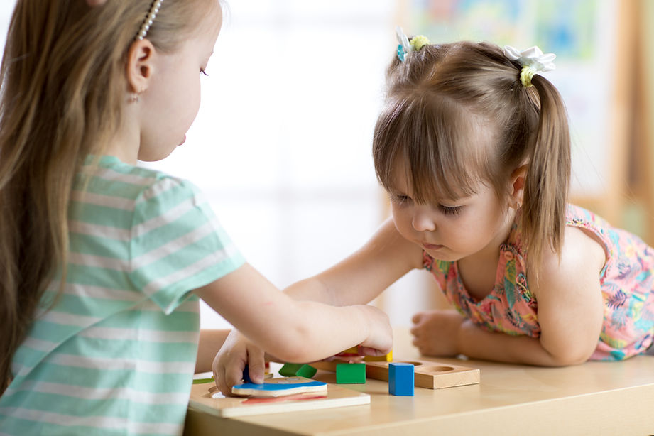 Two toddlers playing with wooden shape puzzles at a table.