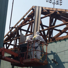 Workers in hazmat suits on a lift repairing a building roof.