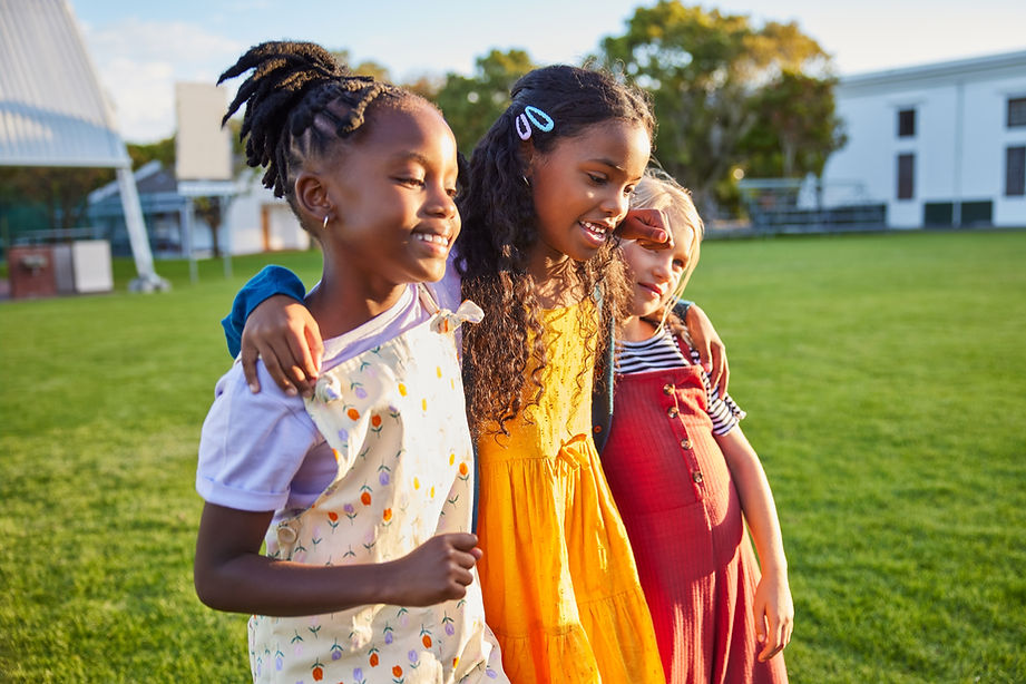 Three young girls smiling and walking on a grassy field.
