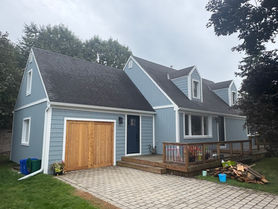 Light blue house with wooden garage doors and paved driveway