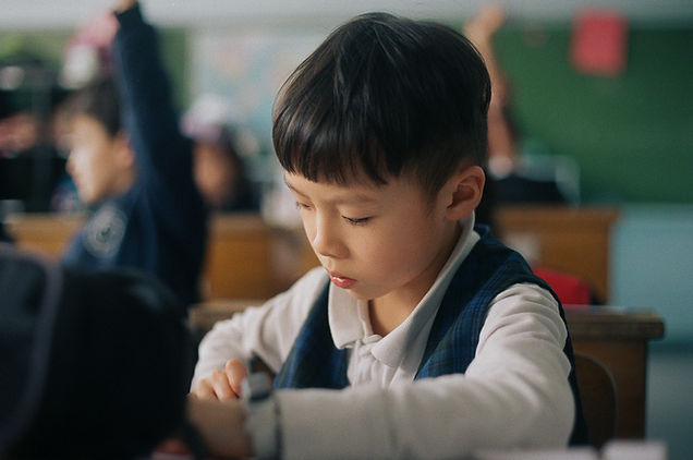 Un petit garçon concentré en classe, regardant quelque chose attentivement.