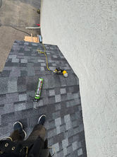 Worker's feet on new dark gray shingled roof with roofing tools.