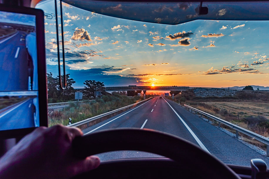 View from the driver's seat of a truck on a highway at dawn with the sun on the horizon an
