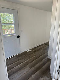 Empty room with white door, dark wood floor, and window view outside.
