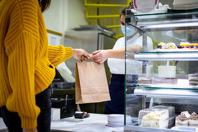 Customer taking shopping bag from cashier in pastry shop.