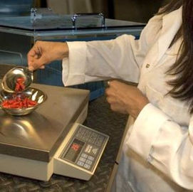 Scientist in a lab coat weighs pills on a digital scale for measurement.