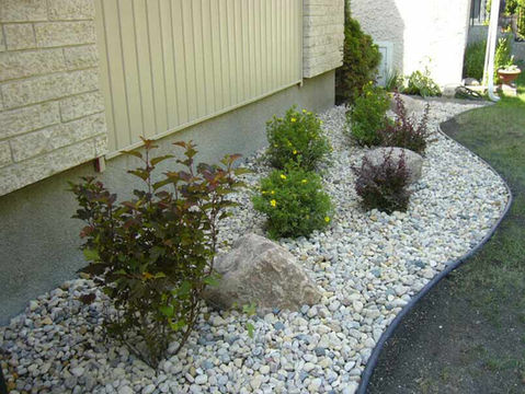 Garden bed with shrubs, rocks, mulch, and decorative stone beside house.