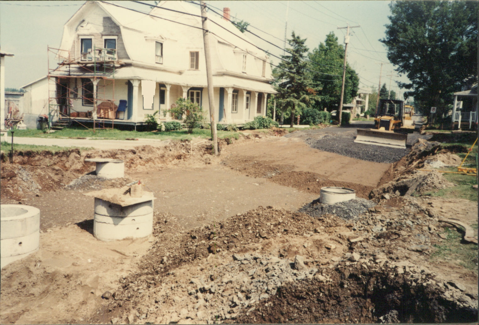 Travaux d'excavation pour infrastructure urbaine devant une vieille maison blanche.