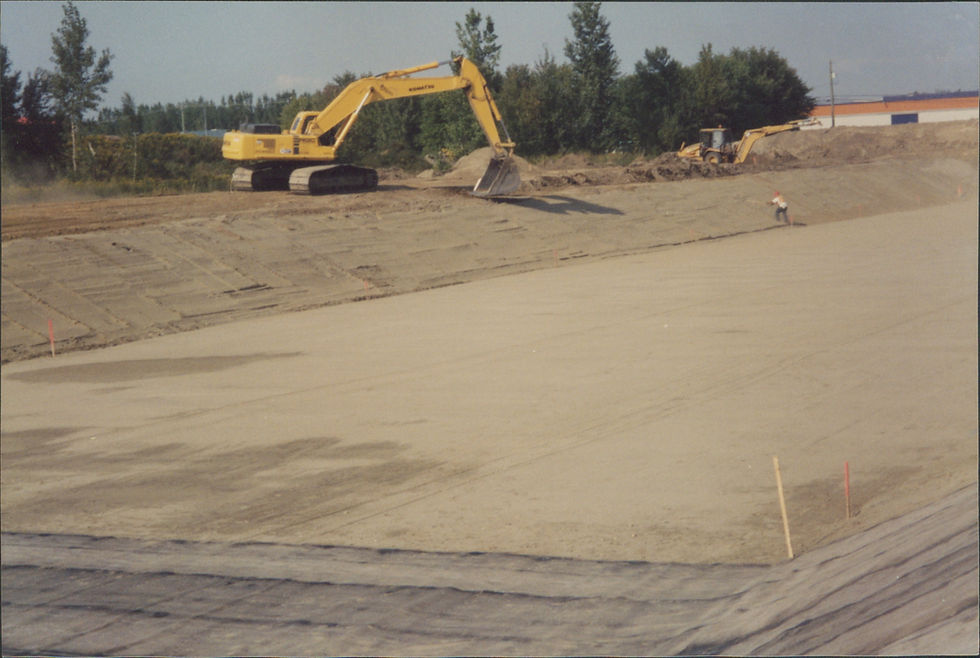 Excavatrice jaune travaillant sur vaste chantier de construction ensoleillé, arbres au loin.