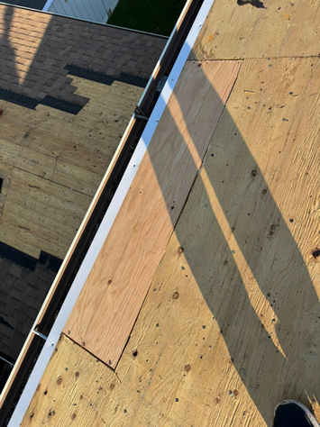 Roof under construction with new shingles and exposed plywood, casting shadows.