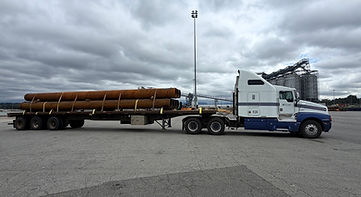 Flatbed semi-truck hauling heavy steel pipes.