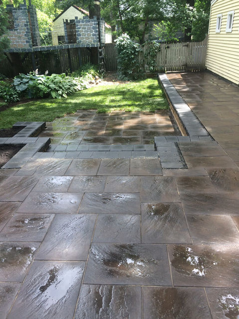 Stone patio with wet surface, green grass, and residential background.