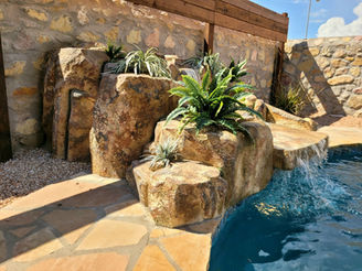 Side angle view of a faux rock waterfall, highlighting cascading water and textured rock design.