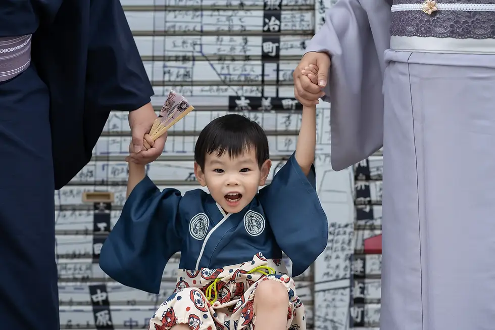 A family of three in kimonos strolling under colorful carp streamers (Koinobori) on Taisho Roman Street in Kawagoe.
