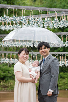 川越市・川越氷川神社での雨の日のお宮参りの出張撮影。フォトスポットの風車の前で相合傘をして写した家族写真。
