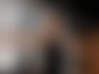 Frau zieht ein rotes Widerstandsband mit ausgestreckten Armen auseinander, im Hintergrund Racks und Turnringe einer Trainingshalle
