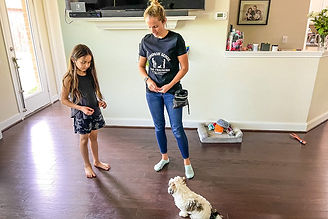 Trainer is showing young girl how to teach her dog to sit inside the home.