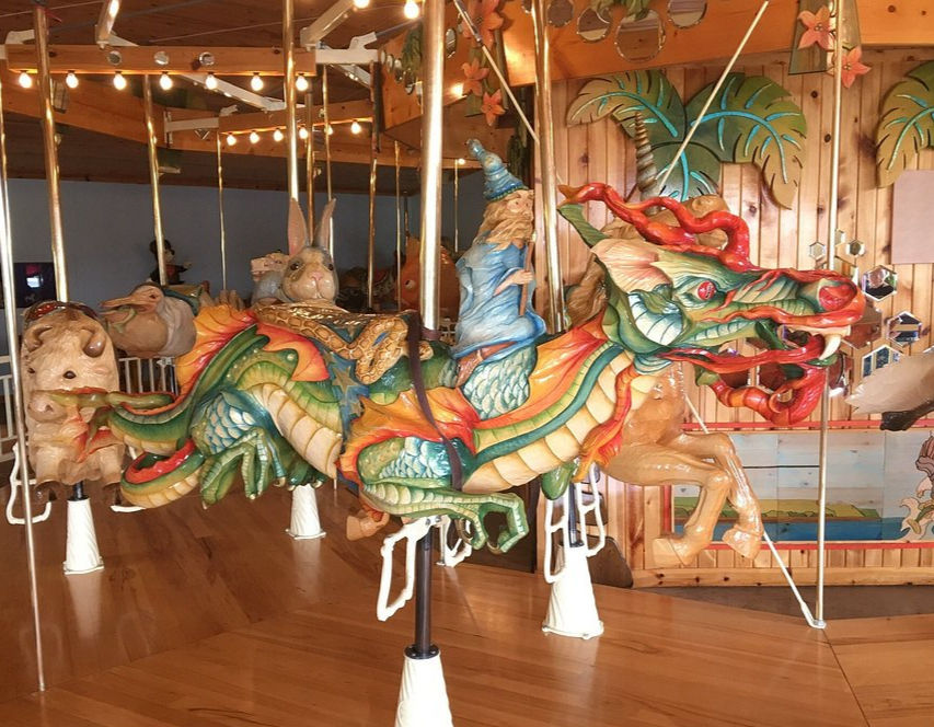 Carousel with colorful dragon, wizard, and animal figures in a wooden, decorated setting. Bright and festive atmosphere.