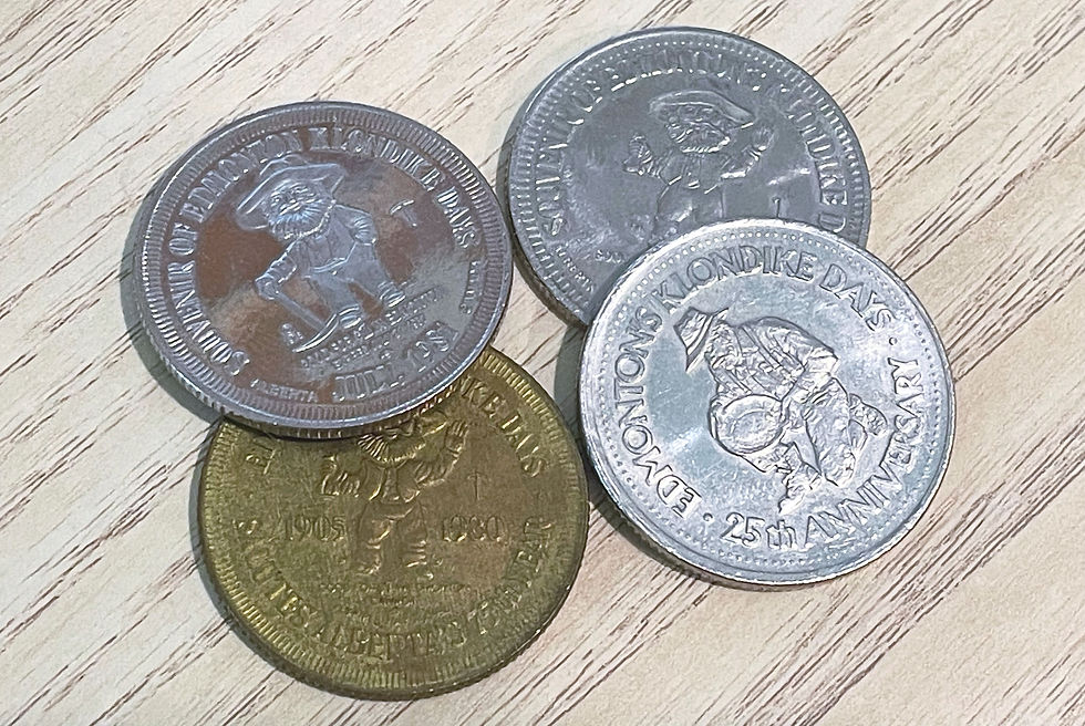 Four coins with Klondike Days inscriptions, featuring prospector figures. Silver and brass tones on a wood-textured surface.