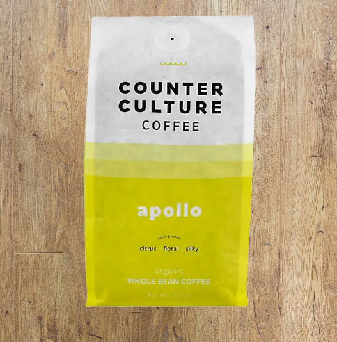 Yellow and white coffee bag labeled "Counter Culture Coffee, Apollo." Descriptors: citrus, floral, silky. Set on a wooden surface.