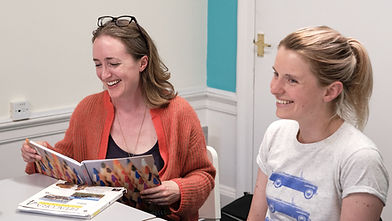 Two adult learners smiling and using a course book during an in-person Spanish class at El Patio in Edinburgh.