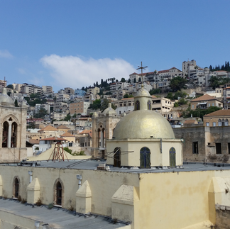 The golden dome of a historic church in Nazareth set against the backdrop of the city's terraced hillside residential buildings.