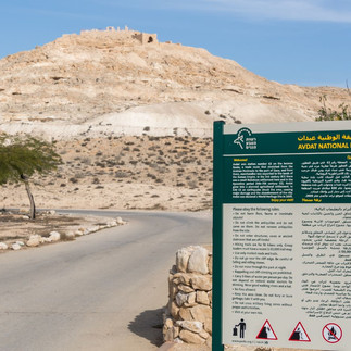 Entrance sign for Avdat National Park with the ancient hilltop ruins in the Negev Desert
