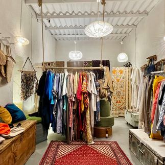 Interior of a luxury boutique fashion store in Neve Tzedek featuring designer clothing and colorful Persian rugs.
