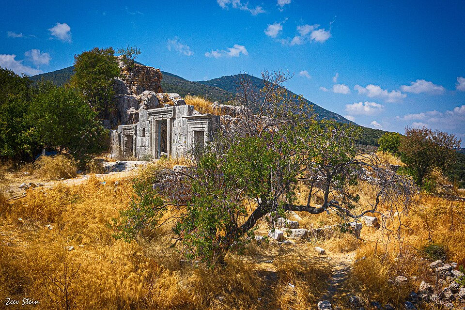 Ancient stone ruins of the Second Temple period Meron synagogue surrounded by dry summer grass under a blue sky in northern Israel.