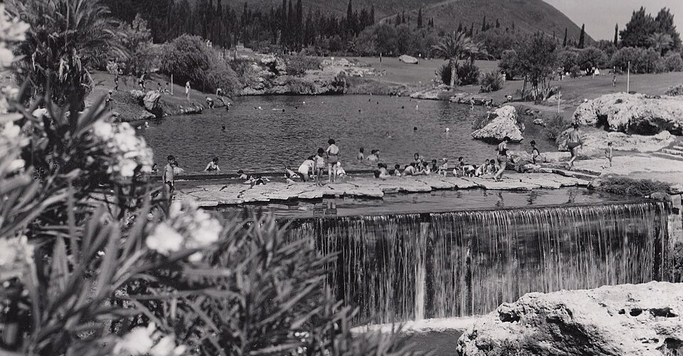 Vintage-style black and white photography of crowds of people swimming above a wide stone waterfall ledge at Sachne.