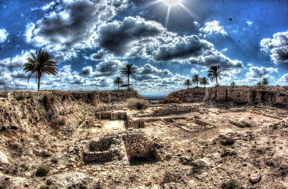 Wide angle panoramic view of the excavated archaeological sectors and historic foundations at Megiddo National Park under dramatic clouds.