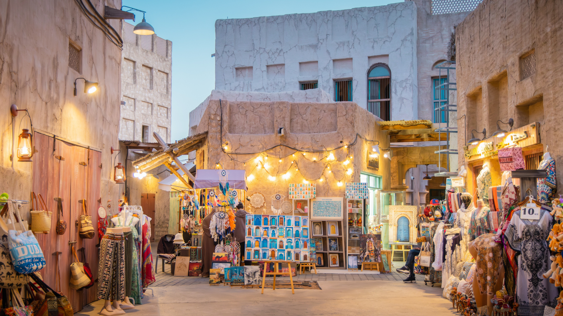 A boutique art and craft stall in Jaffa illuminated by string lights. Hand-painted tiles and local Israeli artwork displayed in a historic stone building.