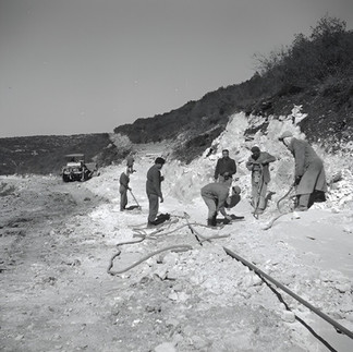Archival black and white photo of workers paved or breaking stone during historical road construction in northern Israel.