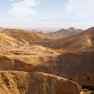 Rolling brown hills of the Judean Desert under a clear blue sky near the Dead Sea.