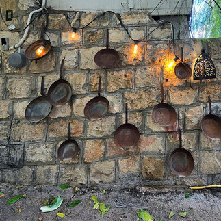 Traditional stone wall decorated with vintage copper pans and rustic hanging string lights in the artistic alleys of Ein Hod Israel.