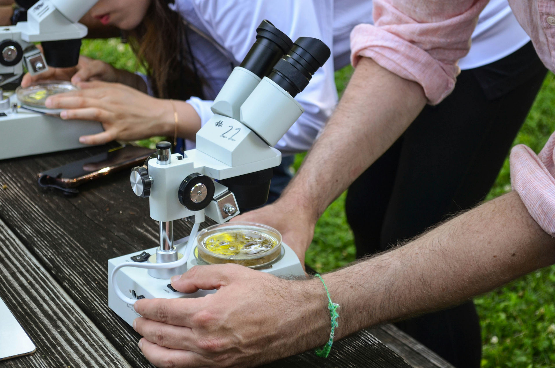 Close-up of students using a professional laboratory microscope during a hands-on outdoor science workshop.