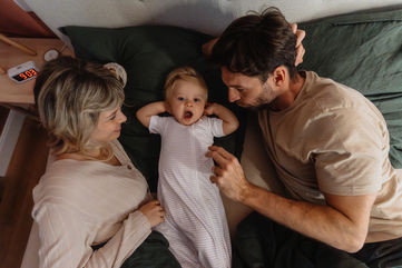 Kleinkind im Bett zwischen den Eltern im Schlafsack