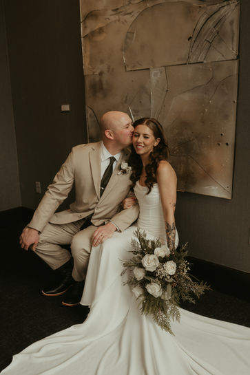 Groom kissing the bride's forehead in front of abstract art