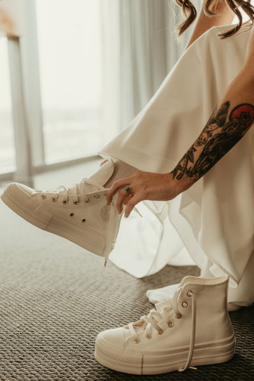 Bride with arm tattoos putting on white platform sneakers