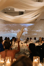 Guests at candlelit dinner with projection screen featuring the coast of Italy